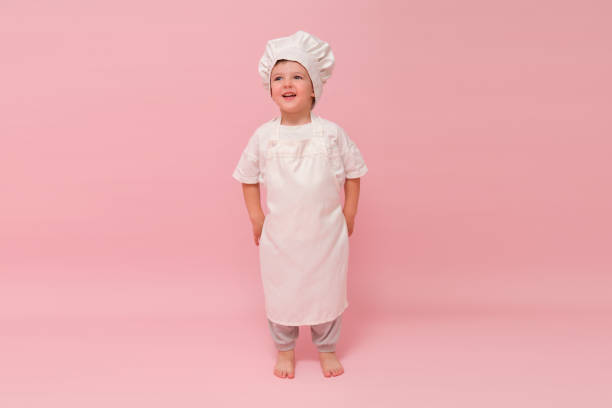 istock A cute child dressed as a chef in a white uniform stands in a studio against a pink background, smiling excitedly. Kid aged 3 years (three year old boy) 2161033015