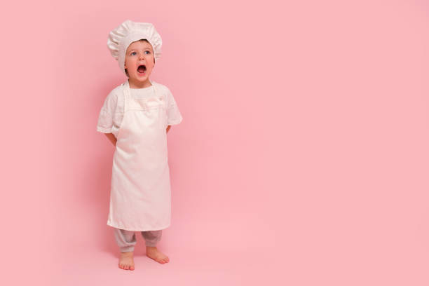 istock Child dressed as a chef in white uniform, studio portrait on pink background. Cooking and culinary concept, full-length photography. Kid aged 3 years (three year old boy) 2161033028