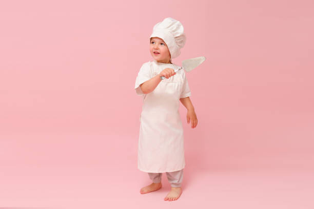 istock A toddler baby dressed as a baker is holding a spatula and showing a funny expression in a studio portrait with a pink background. Kid aged 3 years (three year old boy) 2161033088