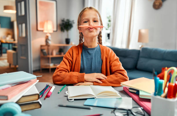 istock Break from studying. Positive pupil with braids sitting by messy table and sticking out lips for making mock moustache 2161043454