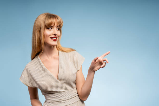 istock Smiling, attractive woman pointing finger at something on blue background 2161044470