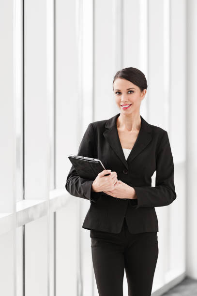 Pretty businesswoman with tablet computer ipad ,wearing black suit with a semi-serious expression in highrise office