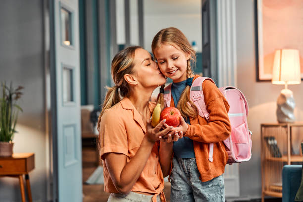 merienda saludable para el alumno. mujer adulta que le da a su hija manzana y plátano para una comida saludable - monoparental fotografías e imágenes de stock