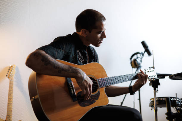 istock Tattooed musician playing acoustic guitar in musical studio 2161051714
