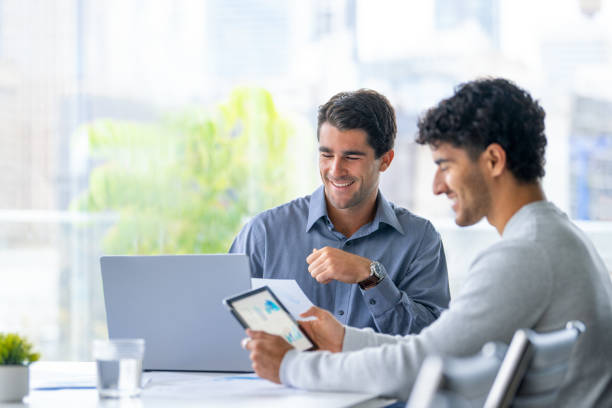Two businessmen working on a digital tablet and laptop computer in the office.