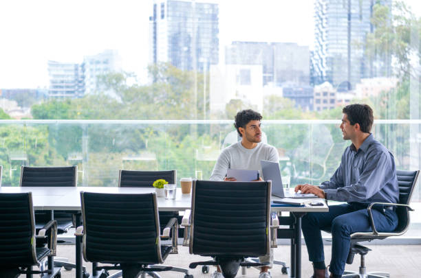 Two businessmen working on a digital tablet and laptop computer in the office a board room or meeting room.