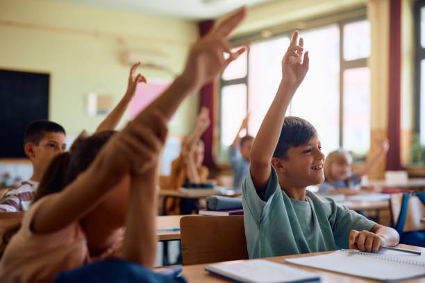 istock Happy boy and his classmates with raised hands during a class at school. 2161063486