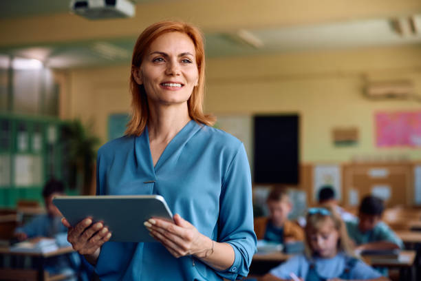 istock Happy female teacher using touchpad in the classroom and looking away. 2161063506