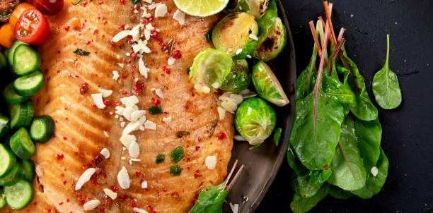 istock Cooked salmon with fresh vegetables, lime and souce. Baked fish on dark background 2161090661