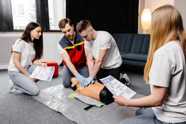istock Young man instructor helping to make first aid heart compressions with dummy during the group training indoors 2161093683