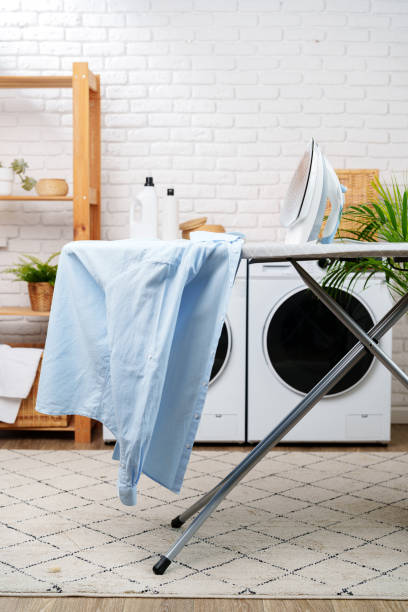 istock White Iron on Grey Ironing Board Next to Laundry Machines in White Room 2161100371