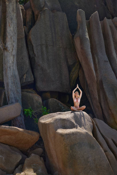 Young woman exercising Yoga with raised arms during summer day on a rock. Copy space.