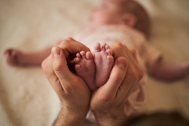Single father is taking care of newborn baby. Close up of his hands and baby’s barefoot forming heart shape.