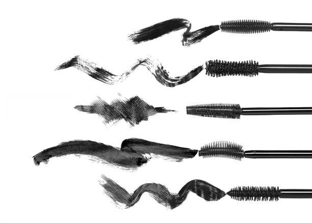 Macro closeupt of a young woman applying mascara with brush on a white studio background