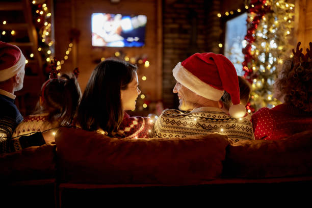 Back view of happy couple talking while watching TV with their family at Christmas night. Rear view of happy couple communicating while watching a movie with their family on New Year's Eve in the living room. typical average stock pictures, royalty-free photos & images