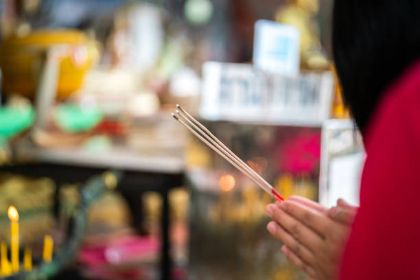 Action of human hand is holding incense stick during making worship at the temple temple. Religion activity scene photo, close-up and selective focus.
