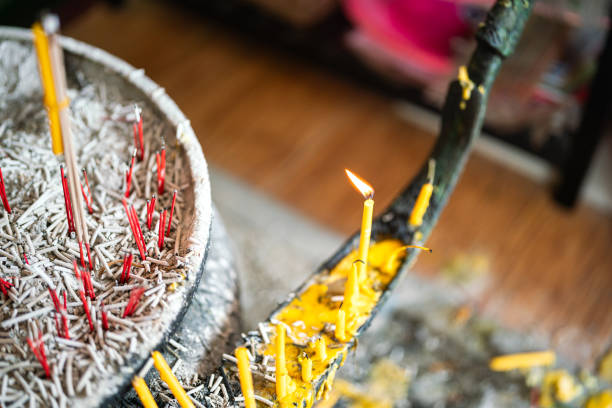 A candle stick with flame is placed on the candle stand in front of Buddha statue at the temple. Close-up and selective focus.
