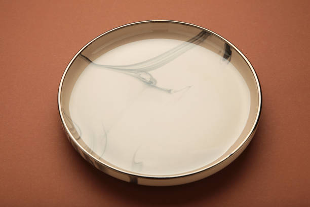 Empty beige ceramic plate on brown background.
