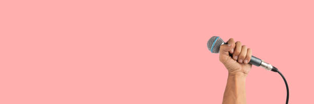 istock Black male hand holding a microphone isolated on pink background 2161118791