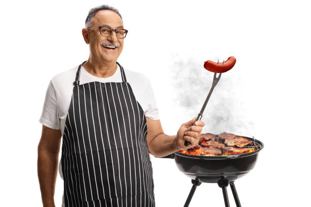 istock Smiling mature man in front of a bbq with a sausage on a fork 2161120408