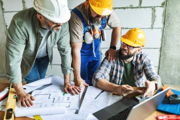 istock Three manual construction workers in hard hats discussing blueprints at construction site 2161121267