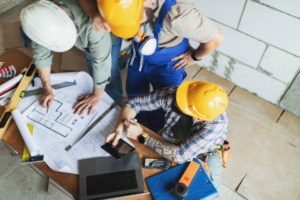 istock Three manual construction workers in hard hats discussing blueprints at construction site 2161121302