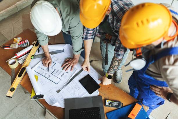 istock Three manual construction workers in hard hats discussing blueprints at construction site 2161121402