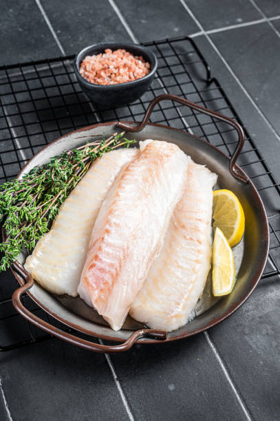 istock Fresh raw cod fish fillets with herbs served on steel tray. Black background. Top view 2161126451