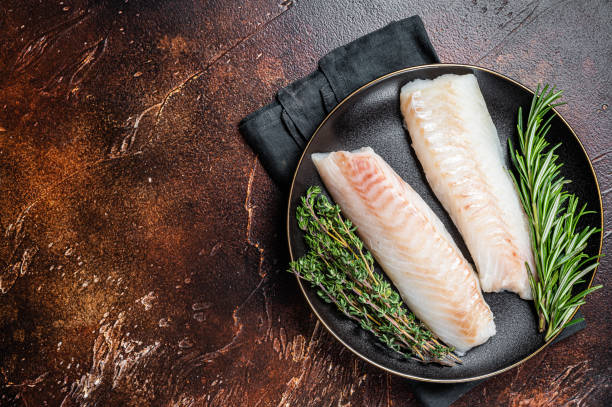 istock Raw cod loin fillet steaks with herbs on plate. Dark background. Top view. Copy space 2161126453