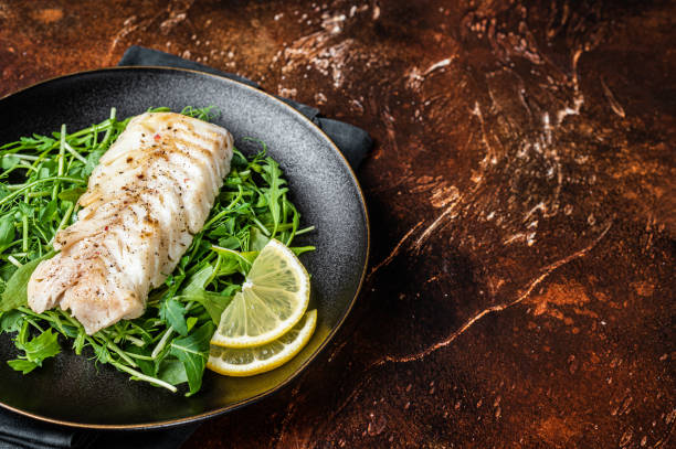 istock Grilled cod fish fillet served with green salad in a plate. Dark background. Top view. Copy space 2161127488