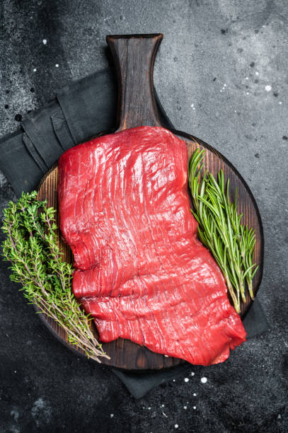 istock Raw flank beef steak, uncooked meat with herbs. Black background. Top view 2161127733