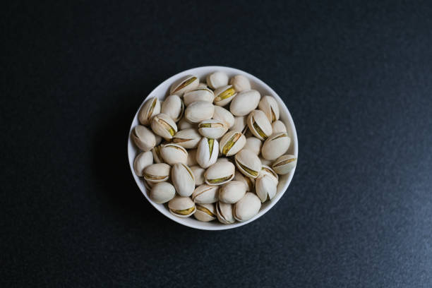 Flat lay of pistachio nuts in white bowl in a morning light and shadow from a window frame.