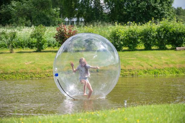 istock Child playing inside a large inflatable ball on a pond with lush greenery in the background 2161135125