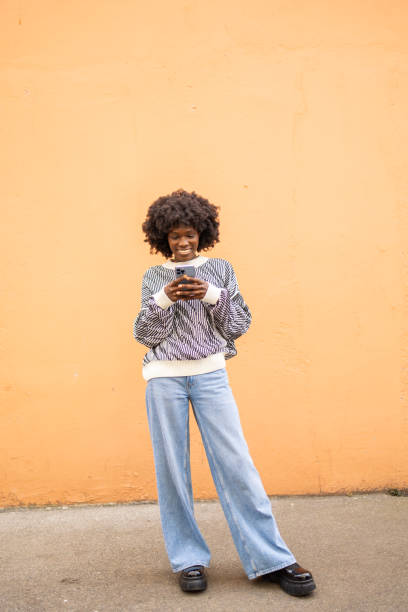 istock Smiling woman texting outdoors against orange background 2161136830