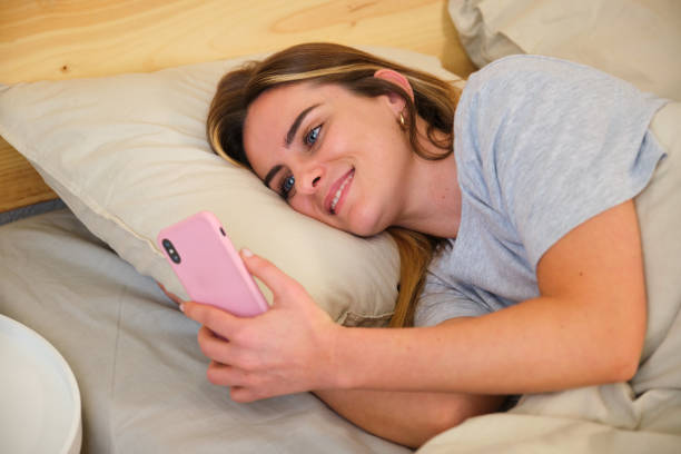 istock Young woman is using smartphone while lying in bed at home 2161142177