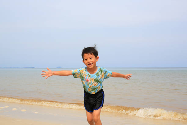 Happy Asian little boy having fun running on tropical sand beach