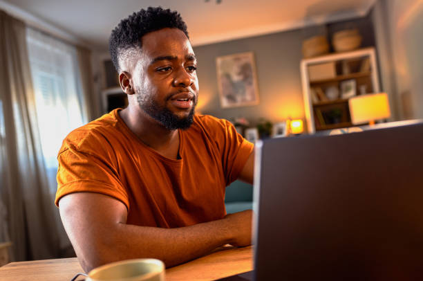 istock Young African American man sitting at home working while using laptop. 2161151942