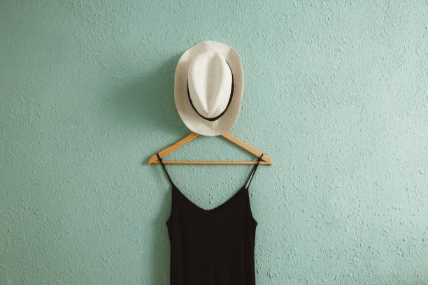 istock Black dress and a summer hat on a hanger with rough old wall background 2161152128