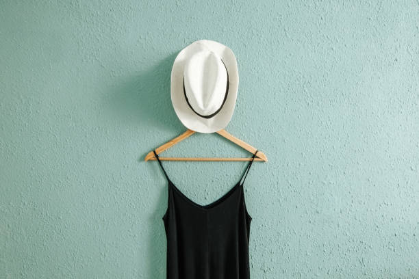 Black dress and a summer hat on a hanger with rough old wall background