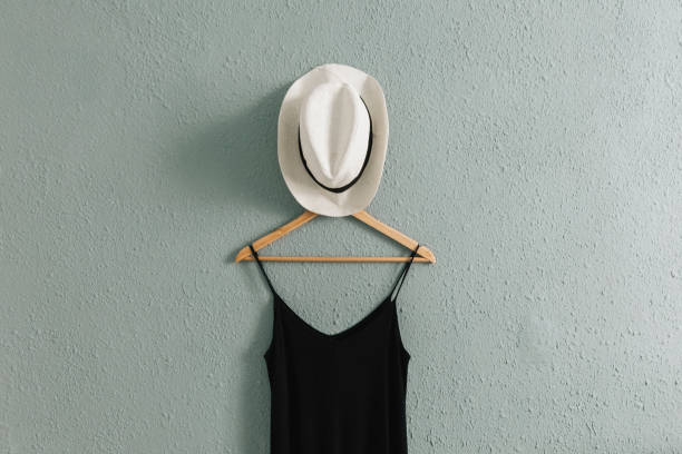 istock Black dress and a summer hat on a hanger with rough old wall background 2161152151