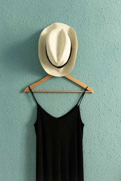 istock Black dress and a summer hat on a hanger with rough old wall background 2161152165