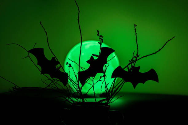 Cutout bats silhouette attached to branches against a green moon. Spooky arts and craft for kids