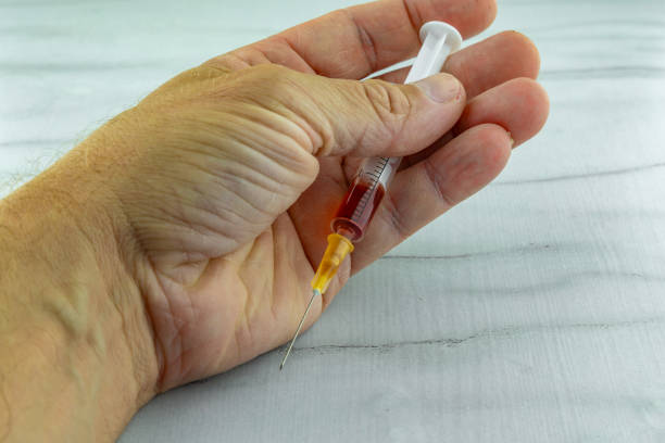 istock Man holds a syringe and sticks a needle into his hand 2161167781