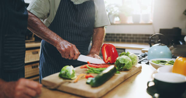istock Hands, people and cutting board in kitchen with help, support and teaching at home for healthy food. Chef with knife for cooking lunch and nutrition with bell pepper, cucumber and green vegetables 2161185515