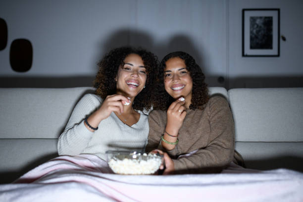 istock Sisters watching TV on sofa: Smiling and laughing 2161190327
