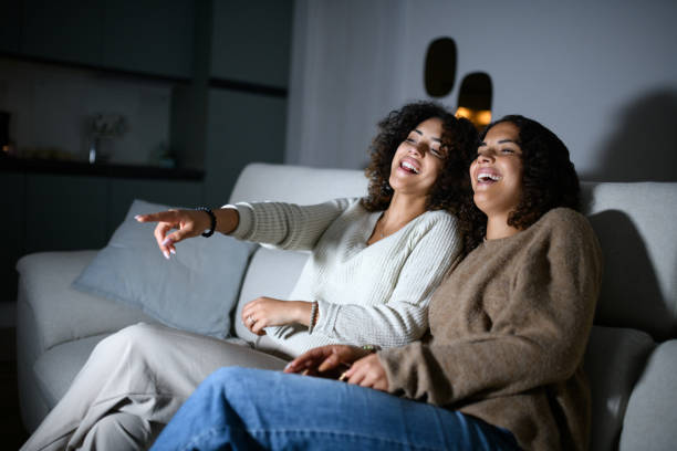 istock Sisters watching TV on sofa: Smiling and laughing 2161190729