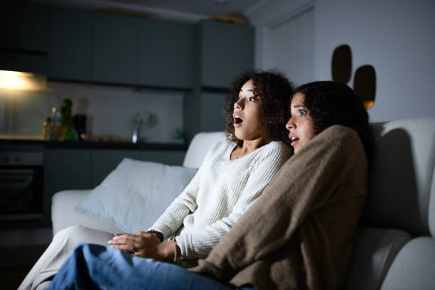 Sisters watching TV on sofa: Scary movie