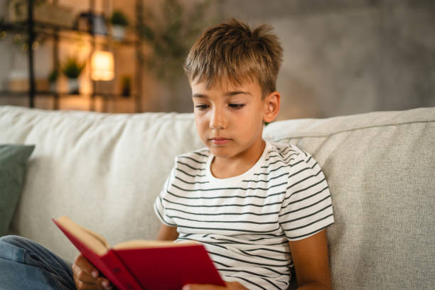 istock young small caucasian boy sit on the sofa and read a book 2161192065