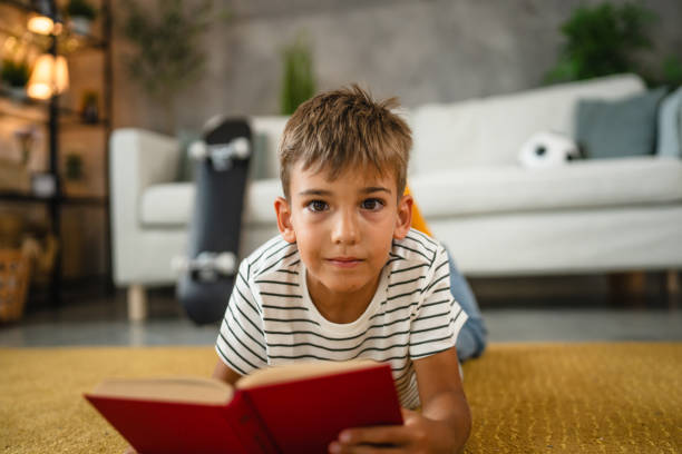 istock young small caucasian boy lying down on the carpet and read a book 2161192165