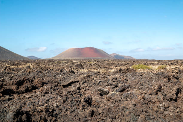 Dry volcanic land. Red Mountain (Montana Roja) on the horizon. Blue sky with white clouds. Lanzarote, Canary Islands, Spain.